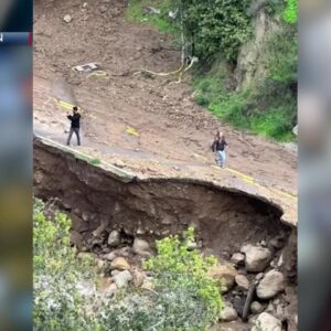 A couple takes pictures as roadway collapses below in Montecito