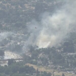 Firefighters battle brush fire near freeway in Granada Hills
